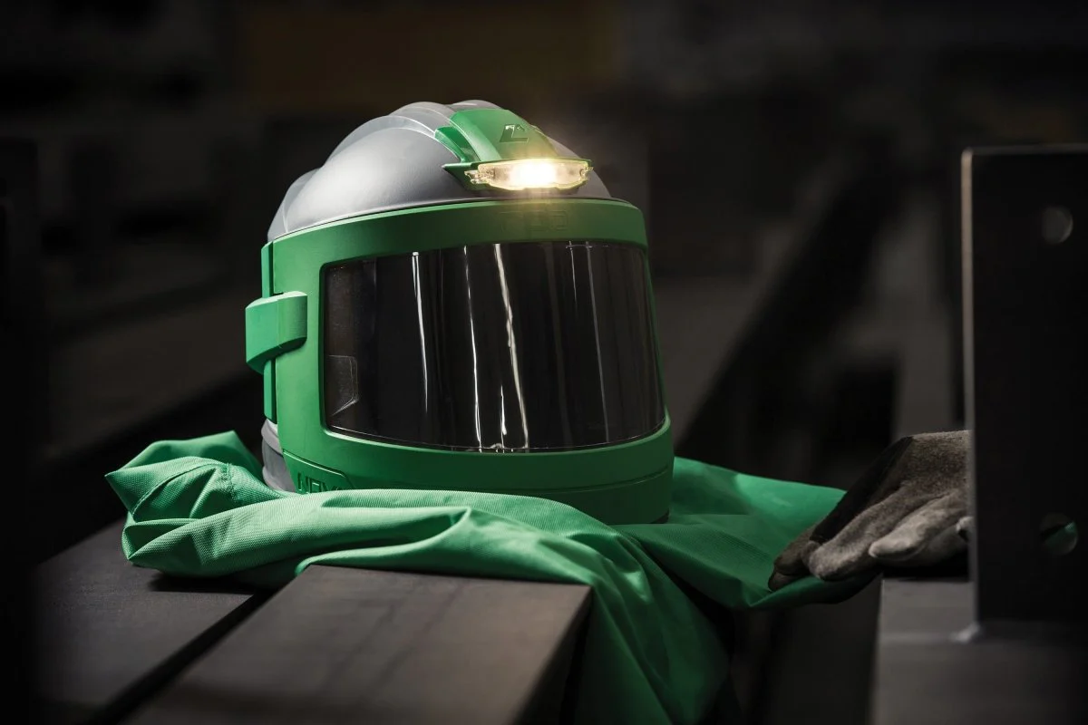 Industrial abrasive blasting helmet, protective gloves, and blasting suit arranged on a steel surface, highlighting essential personal protective equipment (PPE) used for safe surface preparation and sandblasting operations.