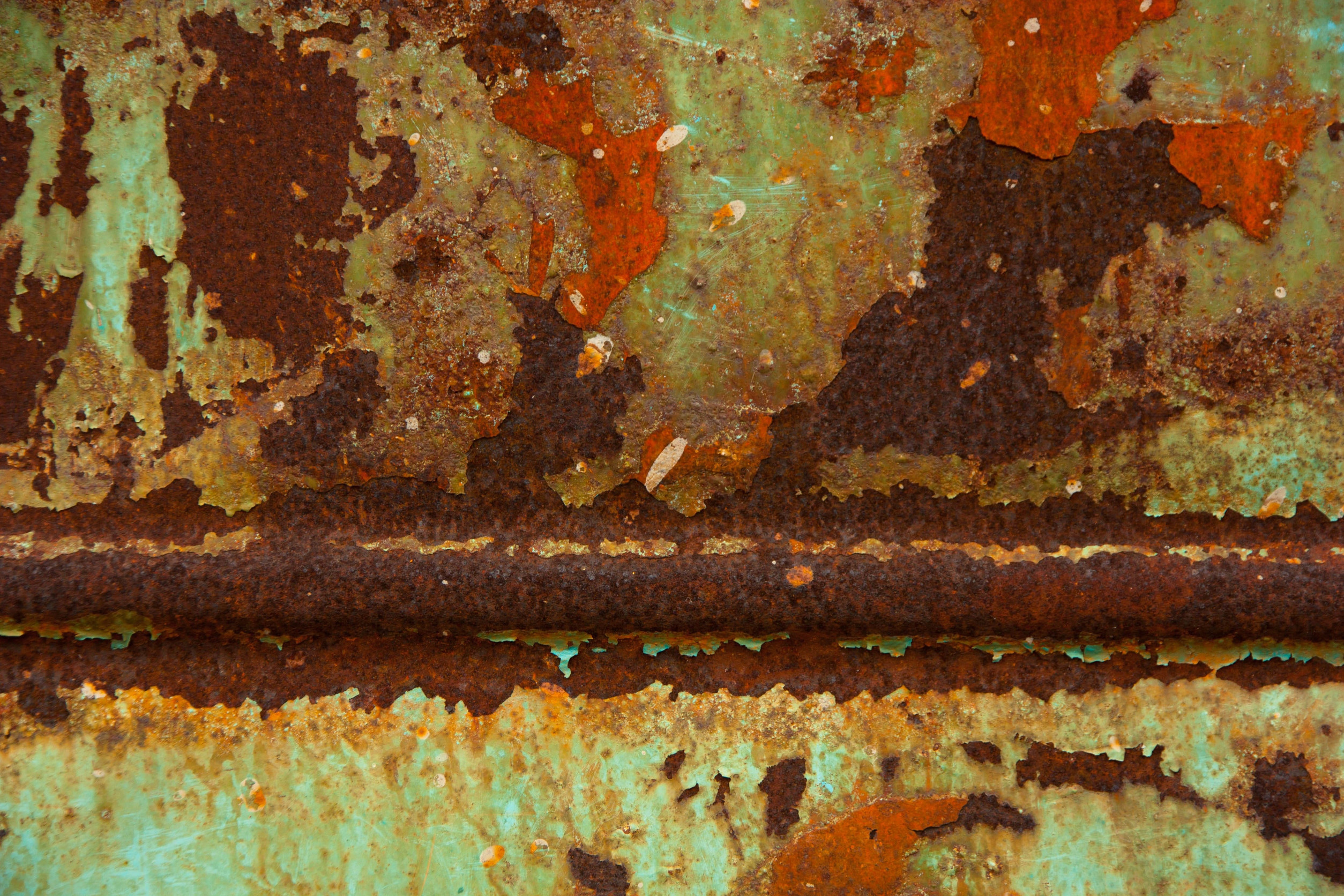 Close-up of heavily corroded, peeling turquoise-green painted metal with extensive reddish-brown rust and flaking layers.