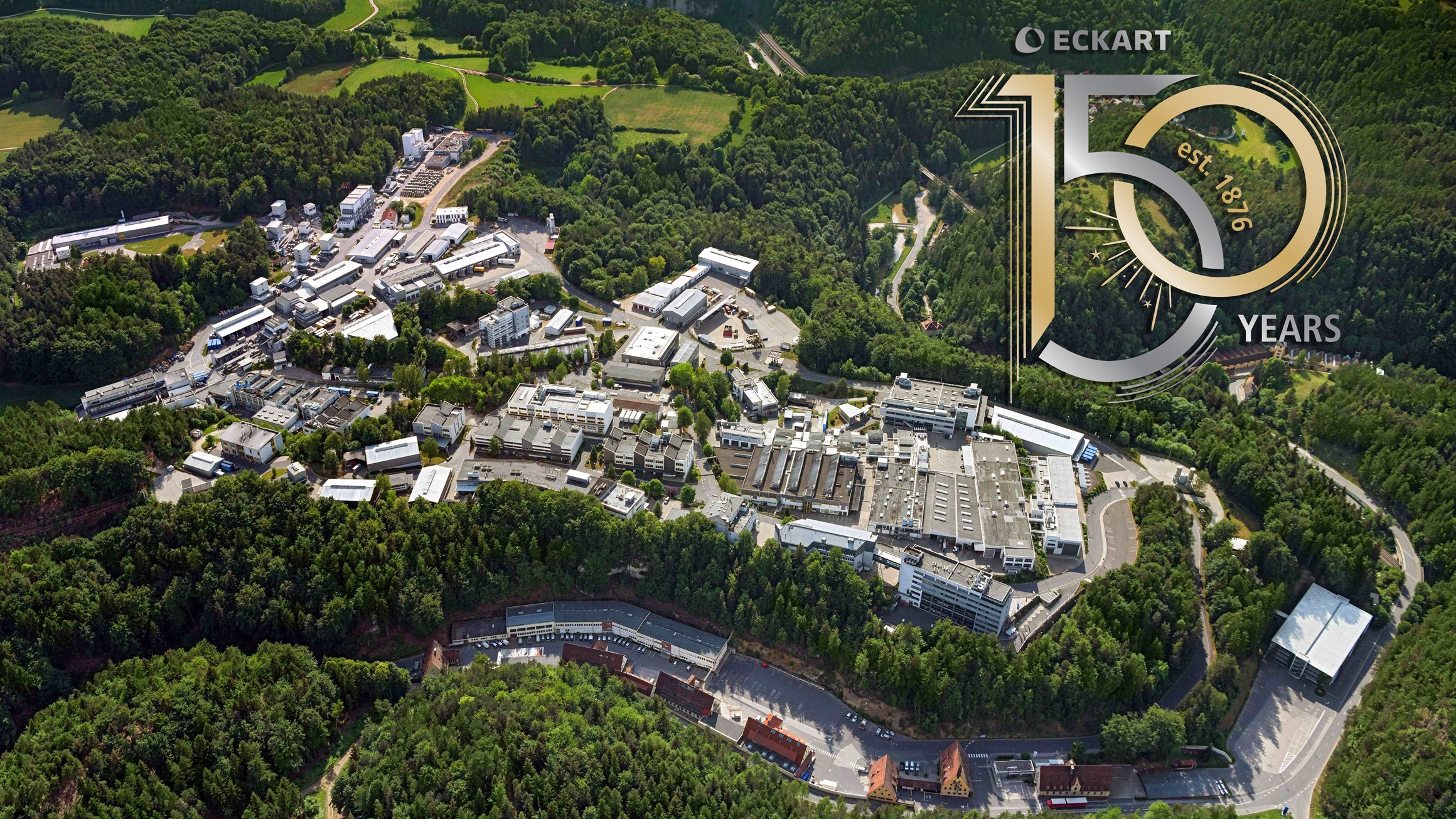 Aerial view of ECKART’s industrial facility surrounded by lush green forests, featuring a prominent 150-year anniversary emblem.