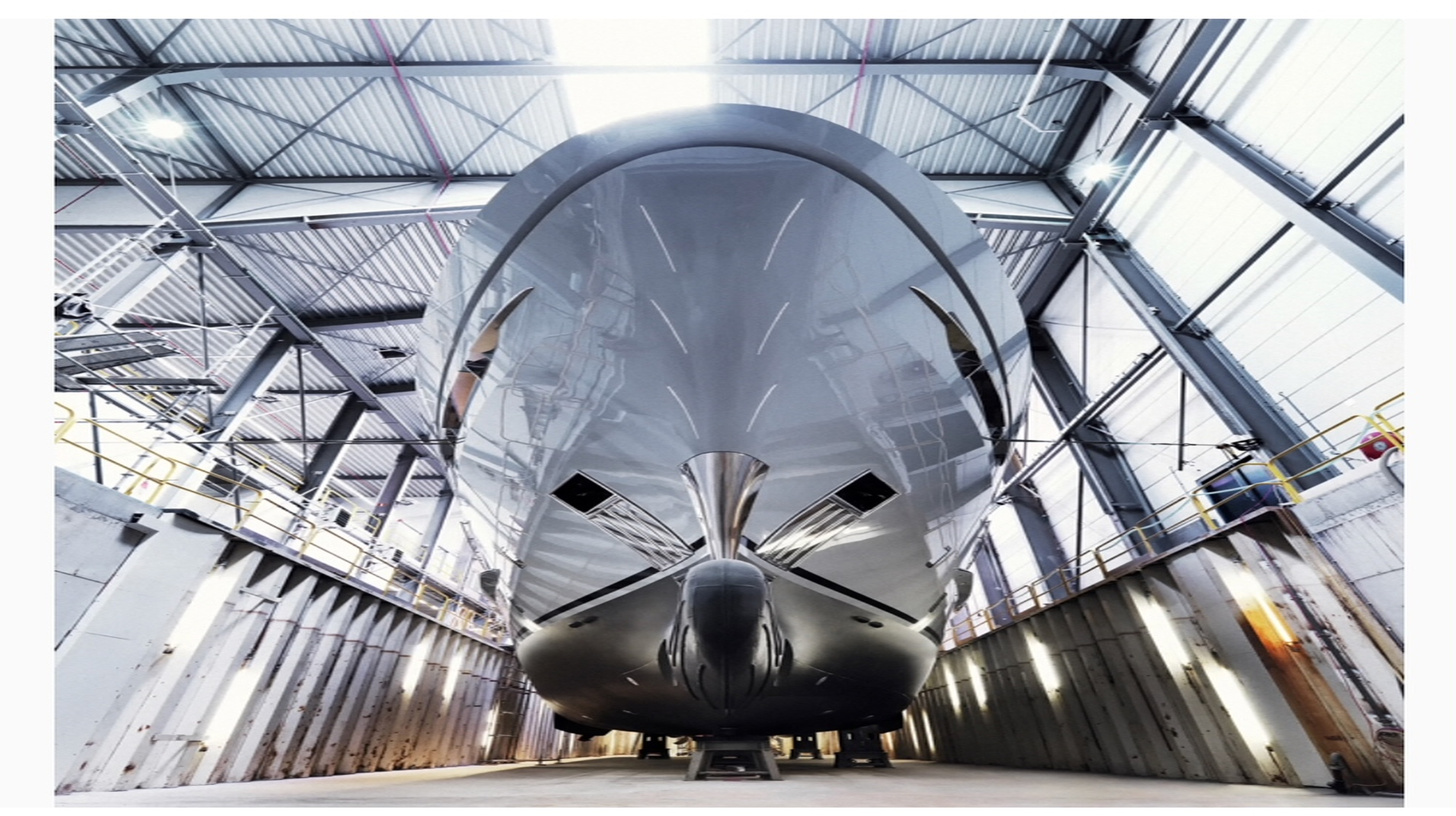 Large white vessel being inspected inside an industrial shipbuilding facility.